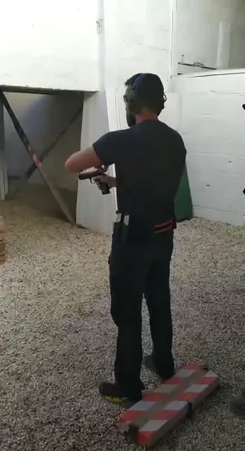 Tirando con pistola en una cancha cubierta de paredes blancas y suelo de grava.